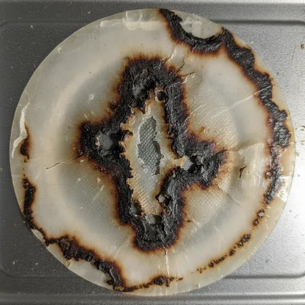 Close-up of a burnt and damaged microwave waveguide cover, showing charring and holes.