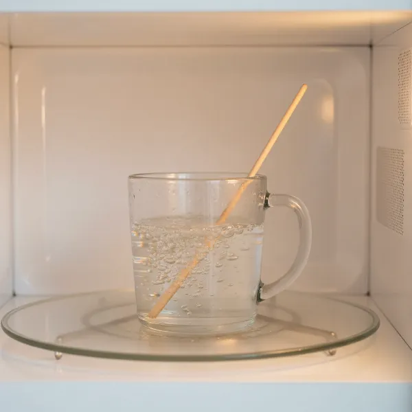 A glass mug in a microwave with a wooden stir stick inside, showing safe water boiling with bubbles.